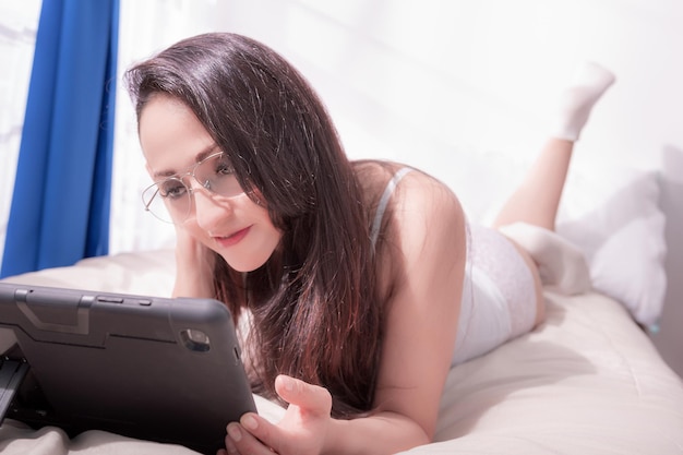 Woman watches her tablet in bed in the morning lots of sunlight coming through her window