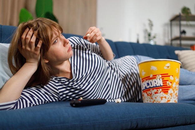 Woman watching a boring movie on tv and eating popcorn