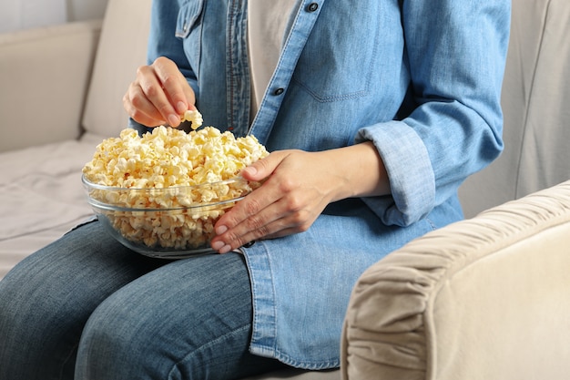 Woman watching film on sofa and eat popcorn. Food for watching films