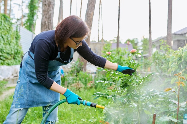 Woman watering plants in a flower bed in the backyard using a hose