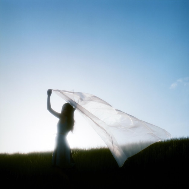 Woman waving scarf on grassy field against sky