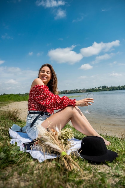 La donna indossa un panno casual che tiene un bicchiere di champagne o vino bianco da solo riposa vicino al lago