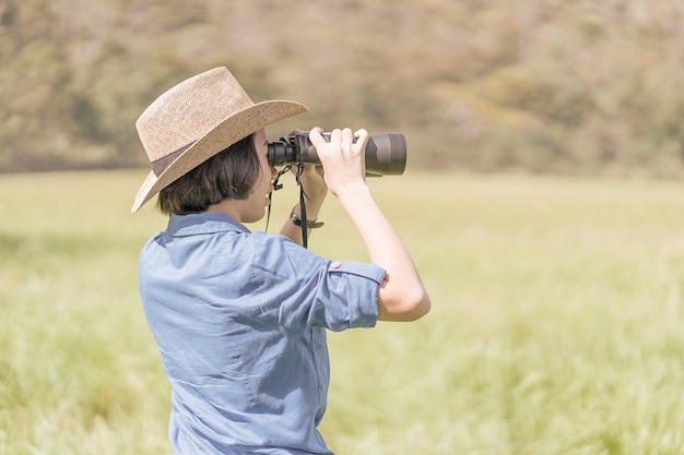 写真 女性は帽子を着用し、芝生のフィールドで双眼鏡を保持