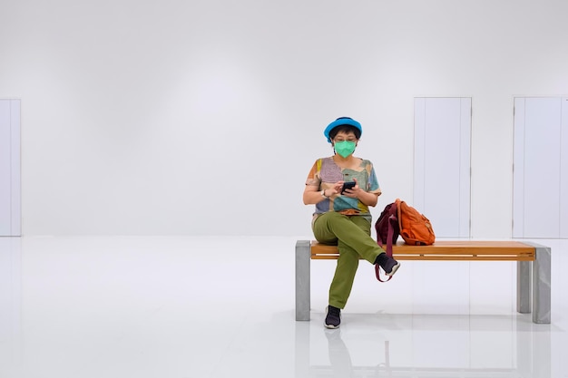 Woman wear protective mask using mobile phone while sitting on bench in rest area of subway station