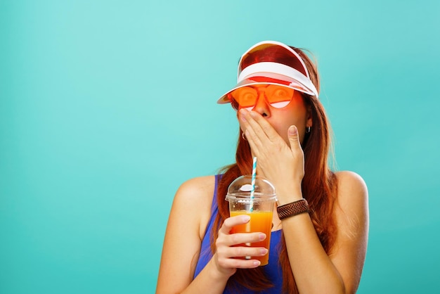 写真 青い水着と帽子をかぶった女性がカップからフルーツジュースを飲む