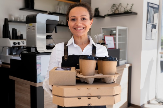 エプロンを着て、パックされた持ち帰り用の食べ物とコーヒーカップを持っている女性