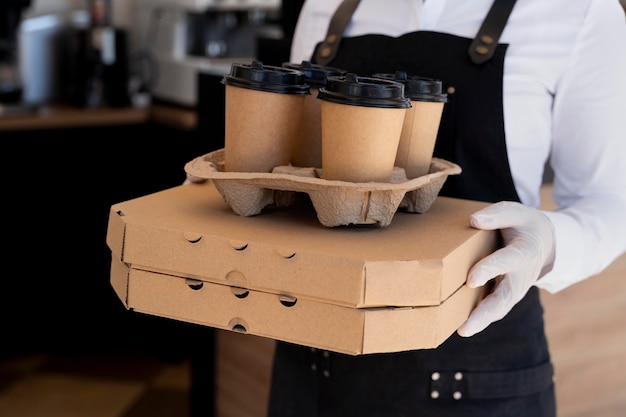 Donna che indossa un grembiule e tiene in mano cibo da asporto e tazze di caffè cup