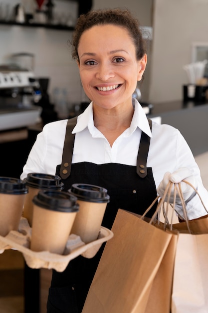 エプロンを着て、持ち帰り用の食べ物とコーヒーカップが入った紙袋を持っている女性