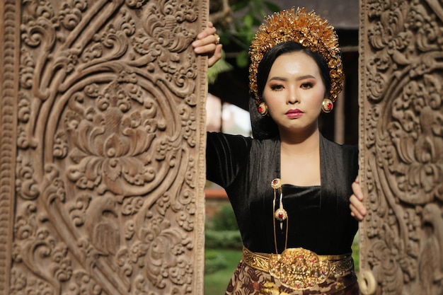 Woman wearing balinese kebaya opens carved wooden door