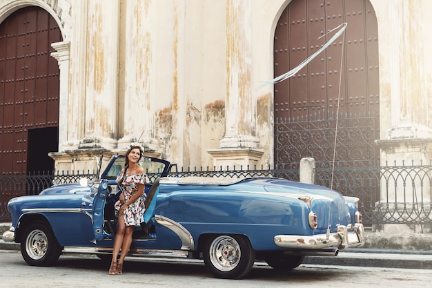 Woman wearing beautiful dress and retro convertible car at Havana city