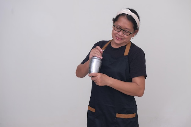 A woman wearing a black apron preparing drink using a shaker