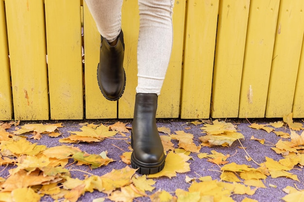 Photo a woman wearing a black boot is walking on the yellow wooden background.