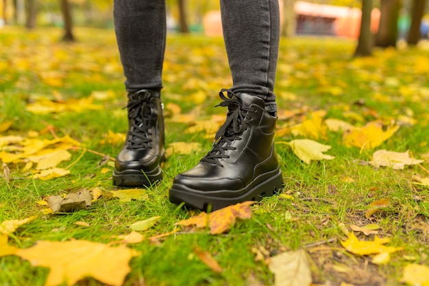 A woman wearing black boots stands on the grass in autumn.