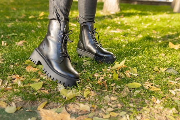 A woman wearing black boots stands on the grass in the fall.