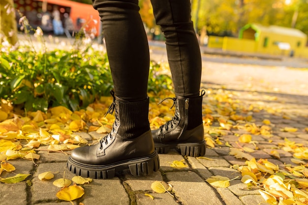 Photo a woman wearing black boots stands on a sidewalk in autumn leaves.