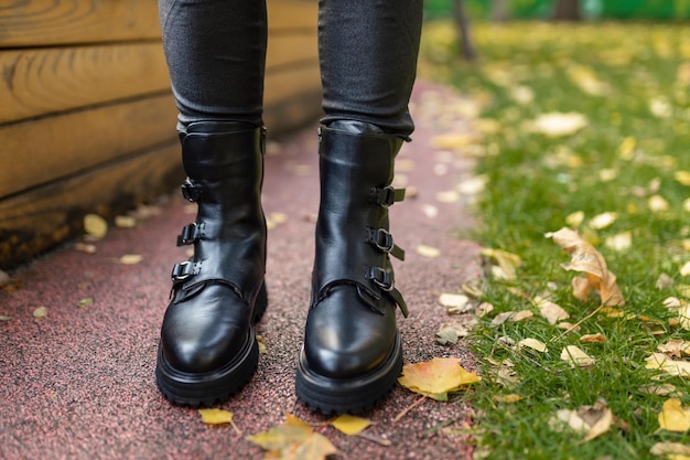 A woman wearing black boots stands on a sidewalk in autumn leaves.
