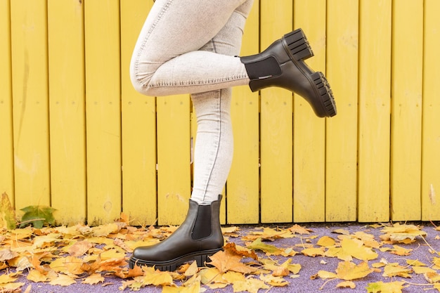 A woman wearing black rain boots stands in front of a yellow wooden wall.