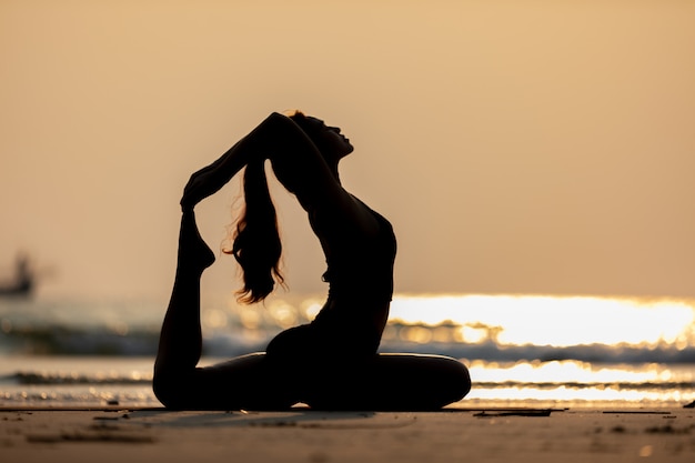 Foto donna che indossa abiti sportivi neri praticando yoga posa sulla spiaggia