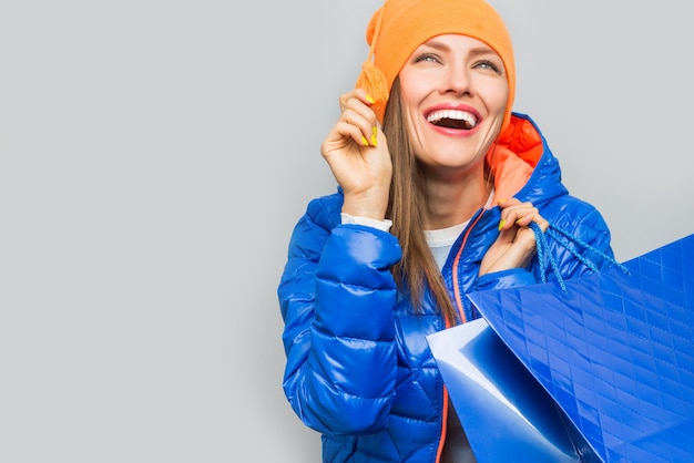 woman wearing blue coat holding shopping bags over grey background