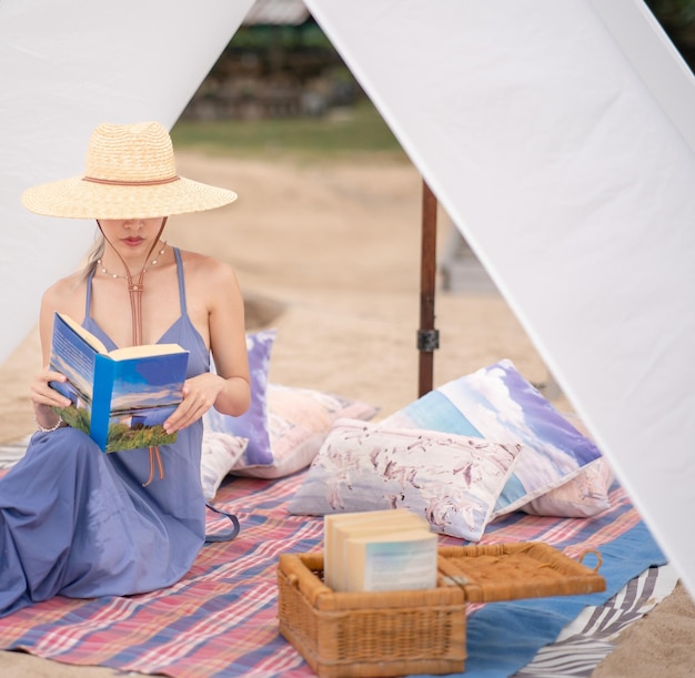 사진 해변의 흰색 텐트 아래에서 책을 읽는 파란 드레스와 밀짚 모자를 쓴 여자