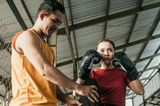 Woman wearing boxing gloves with her trainer standing on the boxing ring