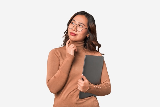 A woman wearing a brown sweater holds a black folder and looks at the camera.