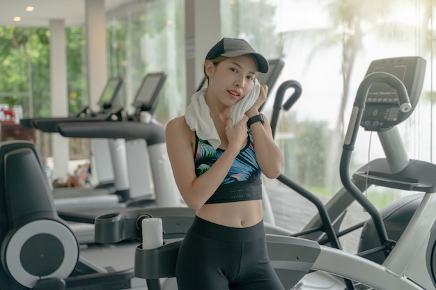 Woman wearing cap having rest while workout in gym. Wipe the sweat with a towel. fitness and sport concept.
