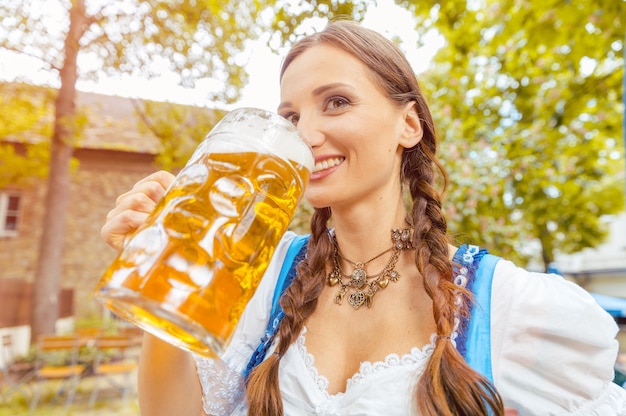 La donna che indossa un abito dirndl sta bevendo birra in una birreria all'aperto bavarese