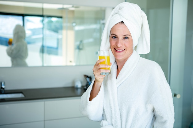 woman wearing a dressing gown and a towel on her head is drinking a glass of orange juice