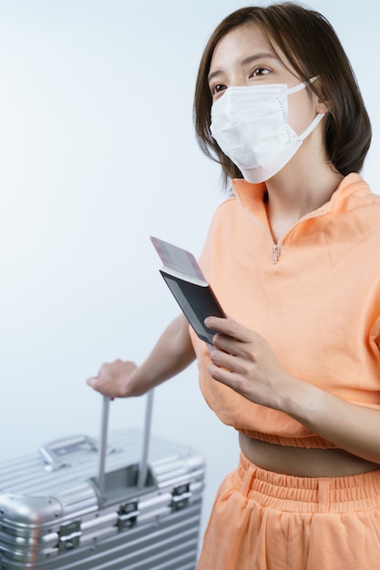 Woman wearing face mask, holding luggage passport