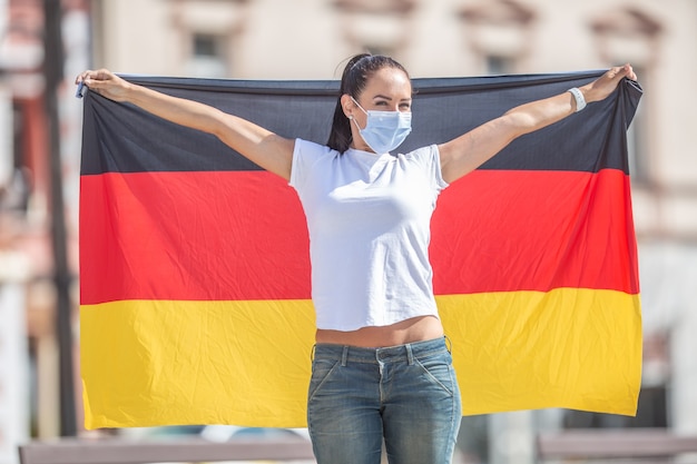 Photo woman wearing a face mask holds a flag of germany behind her.