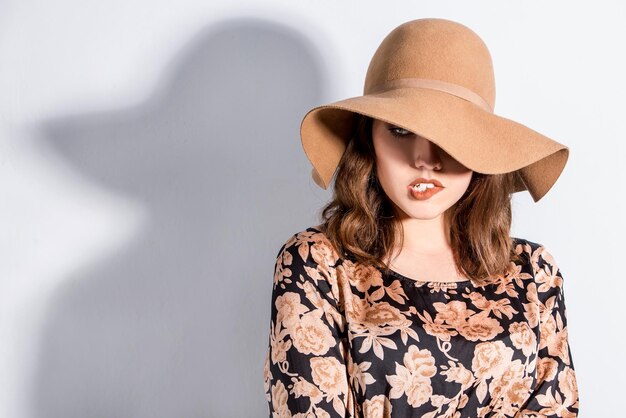 Woman wearing felt hat with a shadow over wall