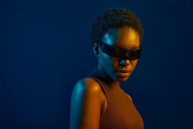 Woman wearing futuristic eyeglasses in neon light over dark studio background