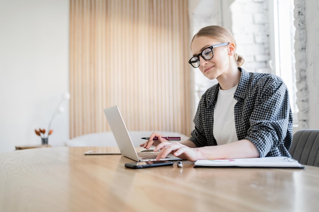 A woman wearing glasses is an online freelancer working in an office workplace using a laptop