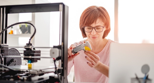 現代の3Dプリンターで作られたプラスチックの詳細を測定する眼鏡をかけている女性