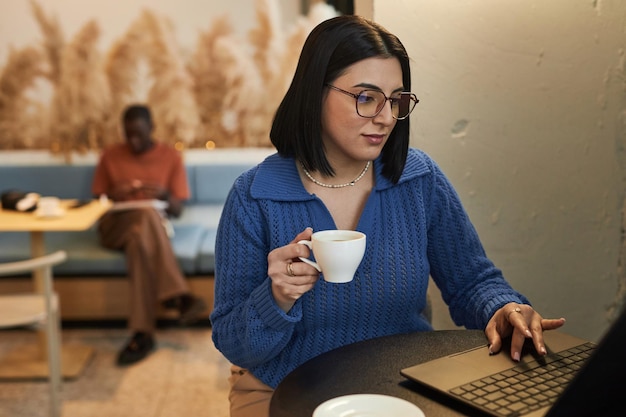 Woman wearing glasses using laptop in coffee shop