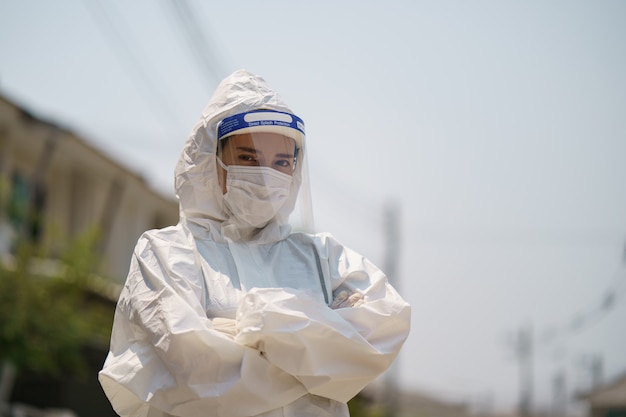 手袋、バイオハザード保護スーツ、顔面シールド、マスククロスアームを身に着けている女性。コロナウイルスまたはCovid-19保護。