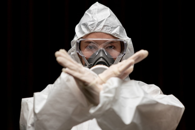 Woman wearing gloves with biohazard chemical protective suit and mask.with unhappy face. woman holds two hands in front of her, sign to stop, stop sign.