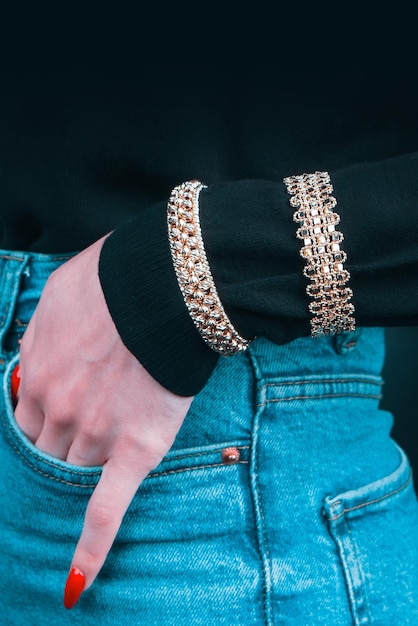 A woman wearing a gold bracelet with a gold chain on the left hand.