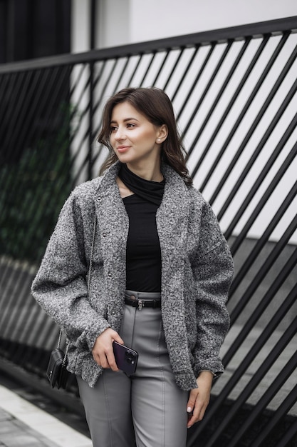 a woman wearing a gray jacket and gray pants is holding a cell phone