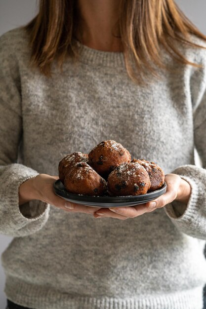 A woman wearing a grey sweater holding a plate of oliebollen Dutch doughnuts dusted with icing sugar