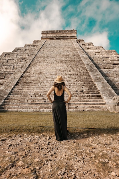 Woman wearing hat and black dress (back view, unrecognized) in front of the Chichen-Itza pyramid in