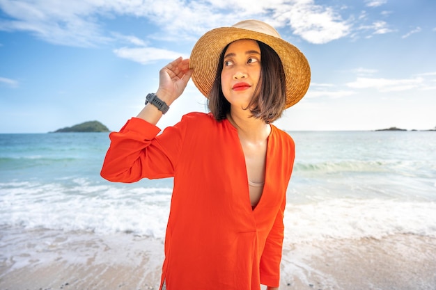 Woman wearing hat looking away while standing at beach against sky