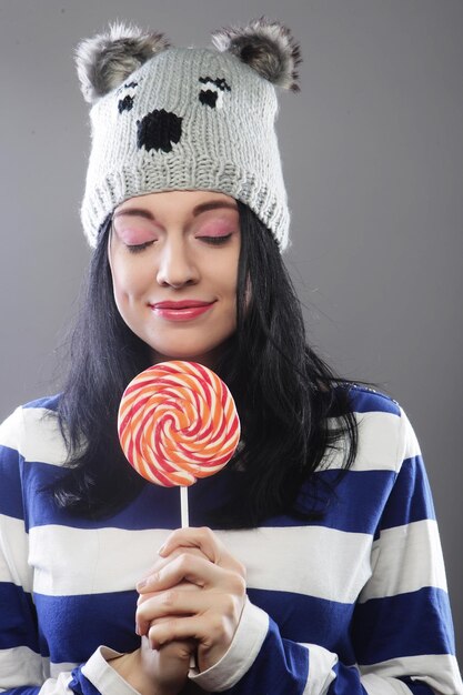 Woman wearing hat looking into the camera and holding a lollipo