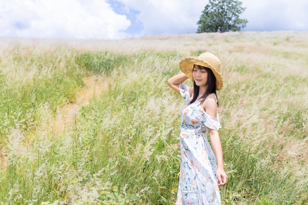 woman wearing a hat, wearing a white dress, standing in the middle of the grass with beautiful white flowers with a relaxed and happy mood.