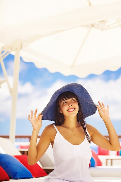 A woman wearing a hat and a white tank top stands under a white umbrella