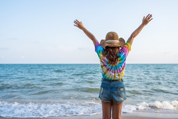 Woman wearing hat with arms raised standing on sea beach