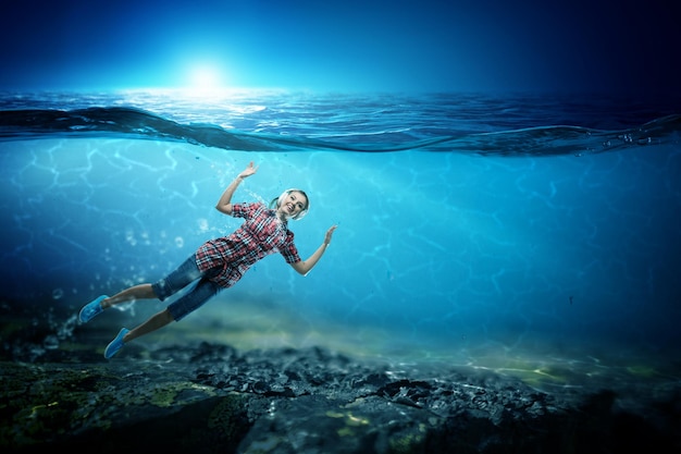 Woman wearing headphones floating underwater. Mixed media