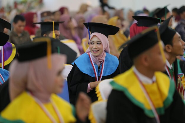 A woman wearing a hijab and cap smiles at the camera