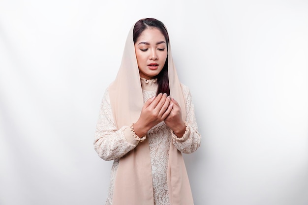 A woman wearing a hijab and a scarf is standing in front of a white background.